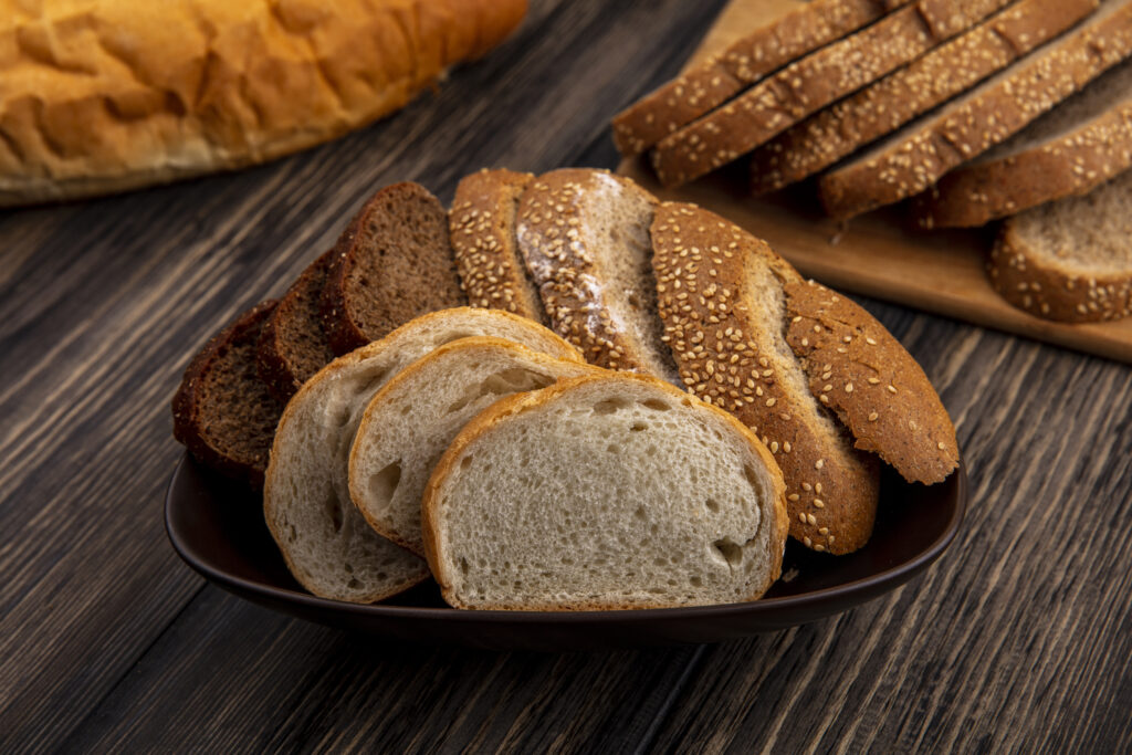 side view of breads as sliced seeded brown cob rye and white ones in bowl and on cutting board on wooden background